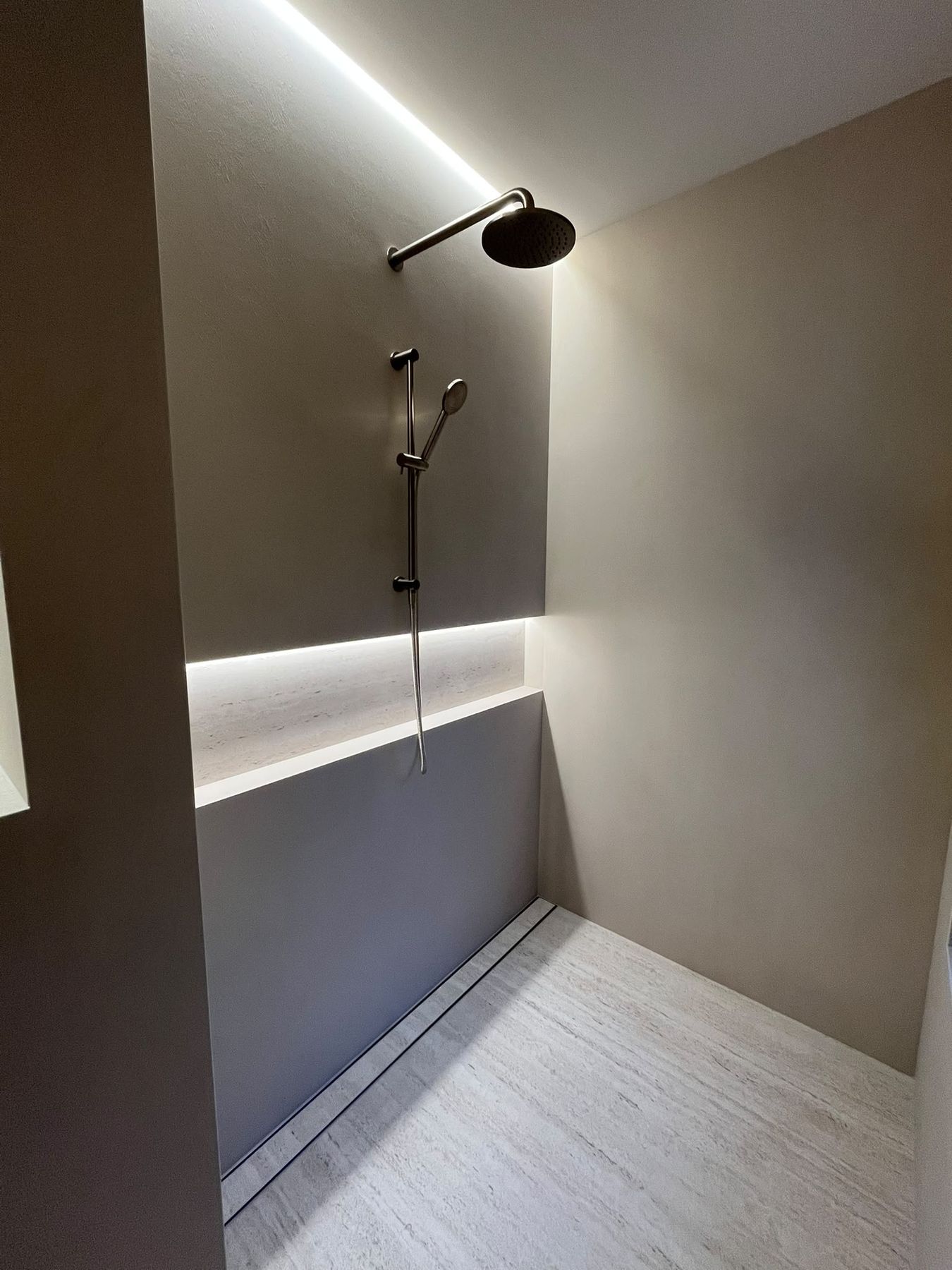 Microcement shower with full-width travertine niche and concealed lighting
